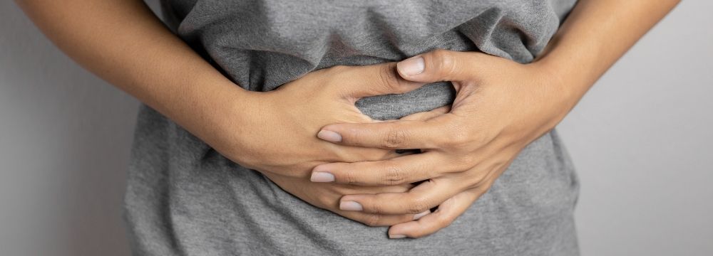 Woman holds abdomen in pain wondering "When is it time to call the doctor for abdominal pain?"