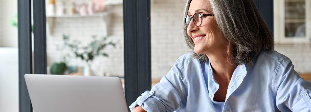 Middle-aged lady sitting at table with open laptop while smiling