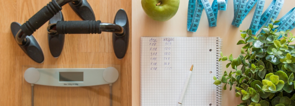 Scale, apple, measuring tape, and dumbells lying on a surface